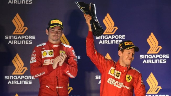 Pebalap Ferrari, Sebastian Vettel (kanan), mengangkat trofi kemenangan F1 GP Singapura di Sirkuit Jalan Raya Marina Bay, Minggu (22/9/2019). Finis kedua ditempati rekan setimnya Charles Leclerc. [AFP/Roslan Rahman]