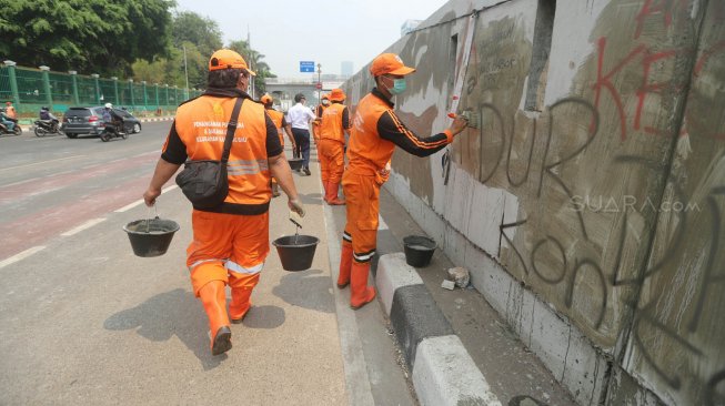 Petugas PPSU membersihkan coretan yang mengotori pembatas jalan pasca unjuk rasa mahasiswa yang berujung ricuh di depan Kompleks Parlemen, Senayan, Jakarta, Rabu (25/9). [Suara.com/Arya Manggala]