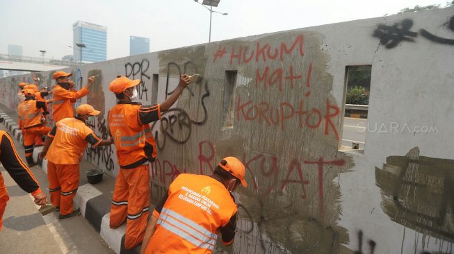 Petugas PPSU membersihkan coretan yang mengotori pembatas jalan pasca unjuk rasa mahasiswa yang berujung ricuh di depan Kompleks Parlemen, Senayan, Jakarta, Rabu (25/9). [Suara.com/Arya Manggala]