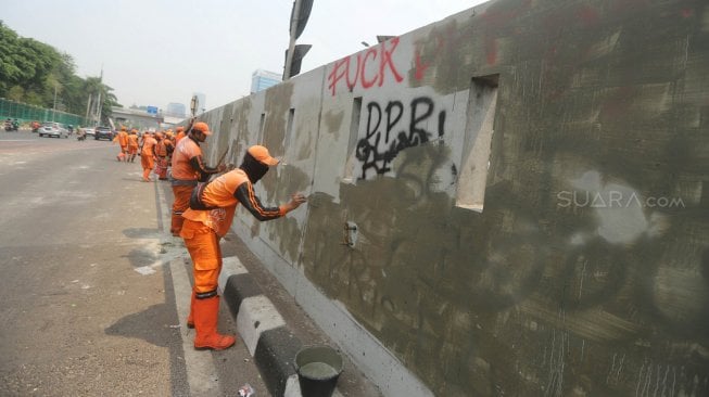 Petugas PPSU membersihkan coretan yang mengotori pembatas jalan pasca unjuk rasa mahasiswa yang berujung ricuh di depan Kompleks Parlemen, Senayan, Jakarta, Rabu (25/9). [Suara.com/Arya Manggala]