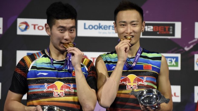 Pasangan ganda putra China, Liu Cheng (kiri) dan Zhang Nan, menggigit medali emas Kejuaraan Dunia Bulutangkis 2017. [AFP/Andy Buchanan]