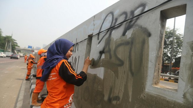 Petugas PPSU membersihkan coretan yang mengotori pembatas jalan pasca unjuk rasa mahasiswa yang berujung ricuh di depan Kompleks Parlemen, Senayan, Jakarta, Rabu (25/9). [Suara.com/Arya Manggala]