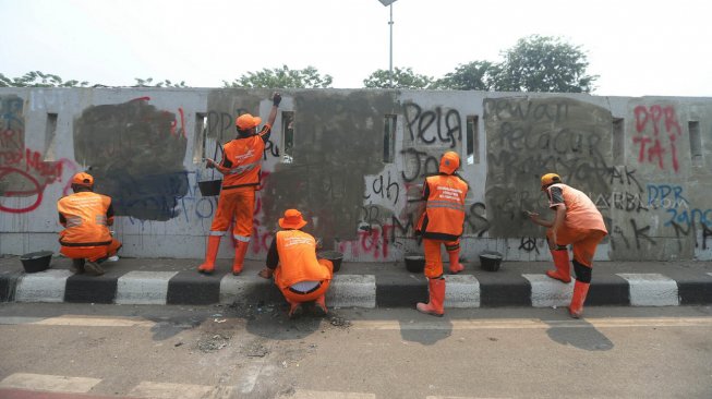 Petugas PPSU membersihkan coretan yang mengotori pembatas jalan pasca unjuk rasa mahasiswa yang berujung ricuh di depan Kompleks Parlemen, Senayan, Jakarta, Rabu (25/9). [Suara.com/Arya Manggala]