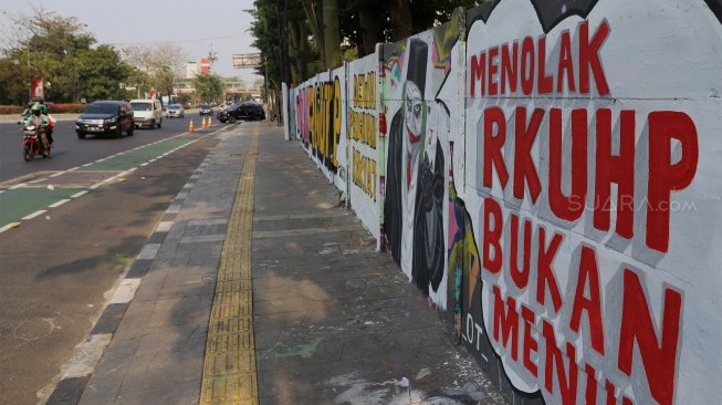 Warga melintas di depan mural bertuliskan "#Tolak RKUHP" di kawasan Rawamangun, Jakarta Timur, Sabtu (28/9). [Suara.com/Angga Budhiyanto]