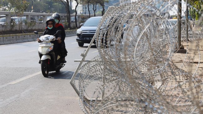 Warga melintas di depan kawat berduri yang terpasang di depan Gedung Badan Pemeriksa Keuangan (BPK), Jakarta, Rabu (2/10).[Suara.com/Angga Budhiyanto]