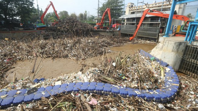 Pekerja dengan alat berat mengangkut sampah yang menumpuk di Pintu Air Manggarai, Jakarta, Rabu (9/10). [Suara.com/Arya Manggala]