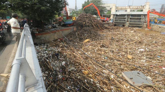 Pekerja dengan alat berat mengangkut sampah yang menumpuk di Pintu Air Manggarai, Jakarta, Rabu (9/10). [Suara.com/Arya Manggala]