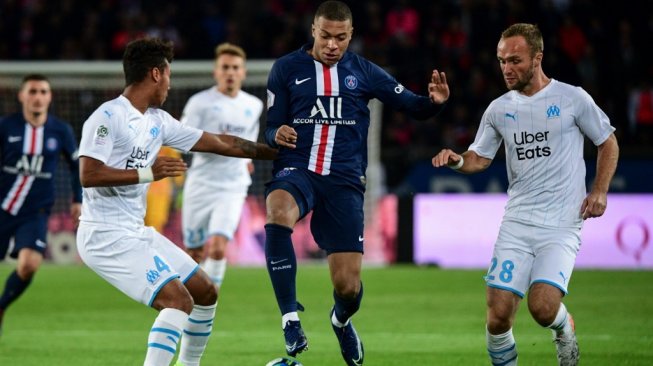 Penyerang PSG, Kylian Mbappe melewati dua pemain Olympique de Marseille pada gelarang Liga Prancis 2019/20 di Stadion Parc des Princes, Senin (28/10/2019)/ [Martin BUREAU / AFP]
