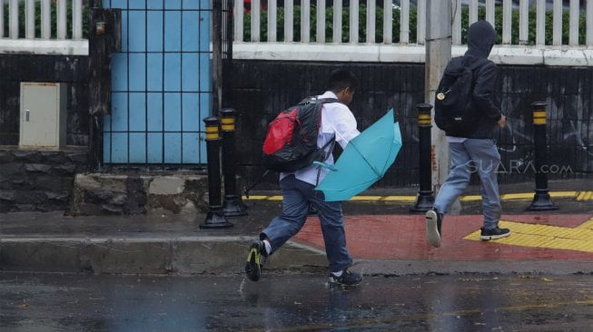 Warga menggunakan payung saat melintas di Jalan Sisisingamangaraja, Kebayoran Baru, Jakarta Selatan, Jumat (1/11). [Suara.com/Angga Budhiyanto]