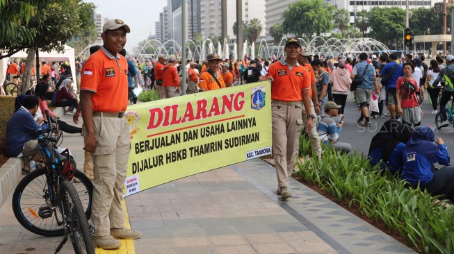 Petugas Satpol PP membentangkan spanduk larangan berjualan di jalur Hari Bebas Kendaraan Bermotor atau Car Free Day, Bundaran HI, Jakarta, Minggu (3/11). [Suara.com/Arya Manggala]