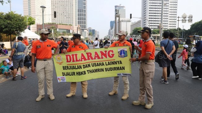 Petugas Satpol PP membentangkan spanduk larangan berjualan di jalur Hari Bebas Kendaraan Bermotor atau Car Free Day, Bundaran HI, Jakarta, Minggu (3/11). [Suara.com/Arya Manggala]