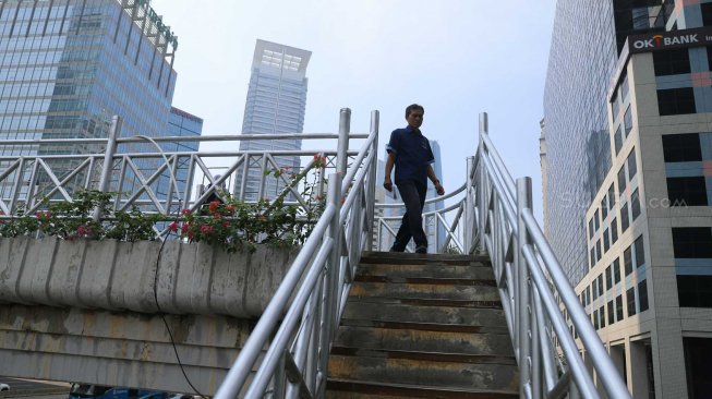 Pejalan kaki melintas di Jembatan Penyeberangan Orang (JPO) tanpa atap di Jalan Sudirman, Jakarta Pusat, Rabu (6/11). [Suara.com/Arya Manggala]
