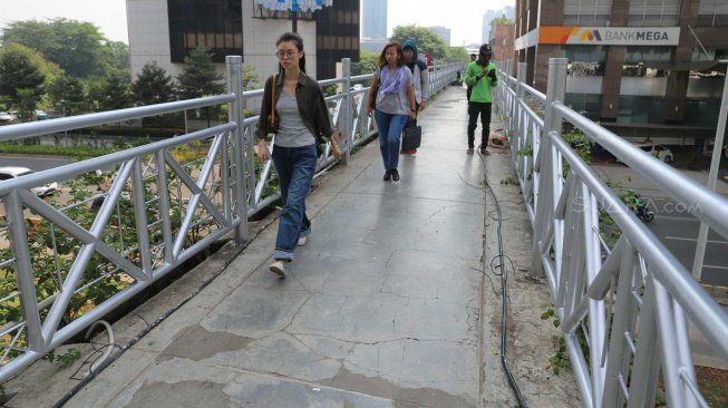 Pejalan kaki melintas di Jembatan Penyeberangan Orang (JPO) tanpa atap di Jalan Sudirman, Jakarta Pusat, Rabu (6/11). [Suara.com/Arya Manggala]