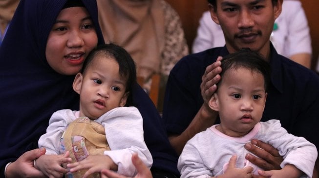 Bayi kembar siam asal Kendari, Sulawesi Tenggara Azila (kiri) digendong ibunya Silvina Dewi dan Aqila (kanan) digendong bapaknya Jayasri di Rumah Sakit Umum Daerah (RSUD) Dr Soetomo, Surabaya, Jawa Timur, Jumat (15/11). [ANTARA FOTO/Didik Suhartono]