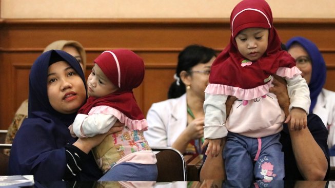 Bayi kembar siam asal Kendari, Sulawesi Tenggara Azila (kiri) digendong ibunya Silvina Dewi dan Aqila (kanan) digendong bapaknya Jayasri di Rumah Sakit Umum Daerah (RSUD) Dr Soetomo, Surabaya, Jawa Timur, Jumat (15/11). [ANTARA FOTO/Didik Suhartono]