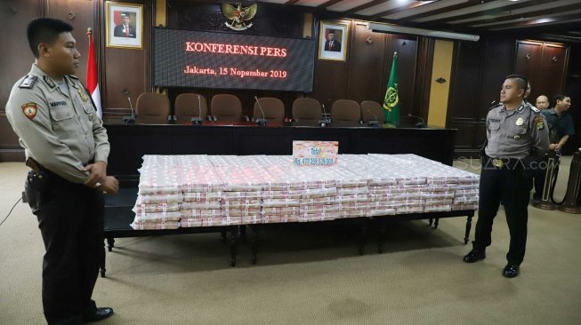 Polisi menjaga barang bukti uang saat konferensi pers di Gedung Kejaksaan Agung, Jakarta, Jumat (15/11). [Suara.com/Arya Manggala]
