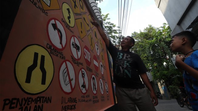 Warga melihat mural edukasi pada tembok di kawasan Pademangan Timur, Jakarta Utara, Minggu (17/11). [Suara.com/Angga Budhiyanto]