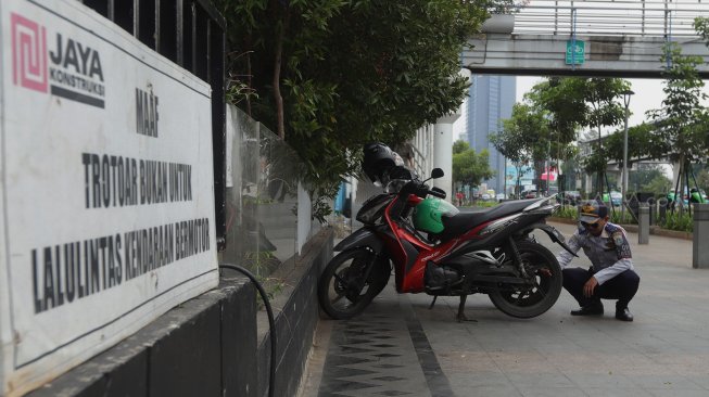 Petugas Dinas Perhubungan (Dishub) DKI Jakarta melakukan penindakan terhadap pengendara yang memarkirkan motor di trotoar di kawasan Sudirman, Jakarta, Jumat (22/11).  [Suara.com/Angga Budhiyanto]
