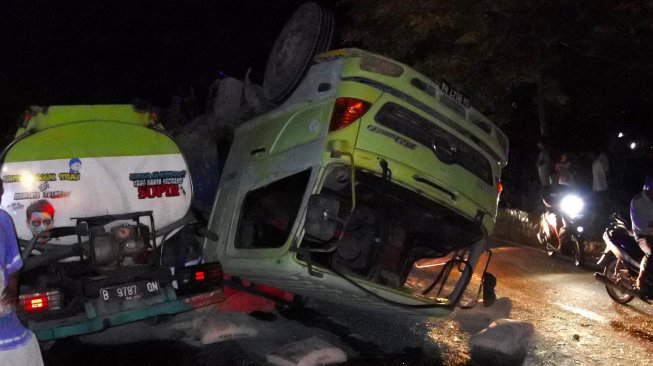 Pengendara bermotor melintas di samping sebuah tronton bermuatan ratusan sak semen terbalik saat mengalami rem blong di Kota Kupang NTT,Sabtu (30/11) malam. [ANTARA FOTO/Kornelis Kaha]
