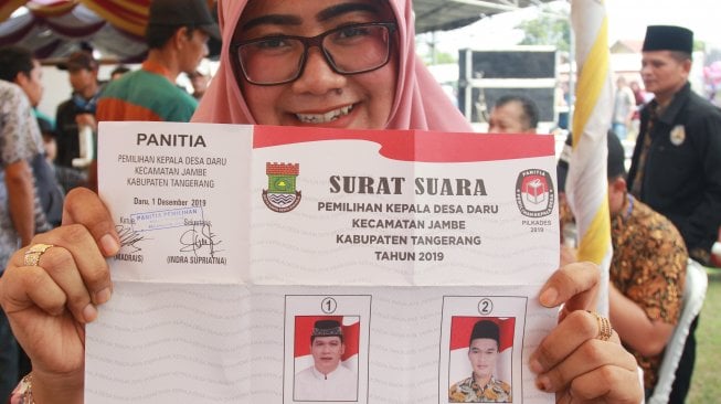 Seorang warga menunjukkan surat suara pemilihan Kepala Desa yang calonnya merupakan anak dan bapak yakni Suharyo (bapak) dan Abdul Malik (anak) di Desa Daru, Kabupaten Tangerang, Banten, Minggu (1/12). [ANTARA FOTO/Muhammad Iqbal]