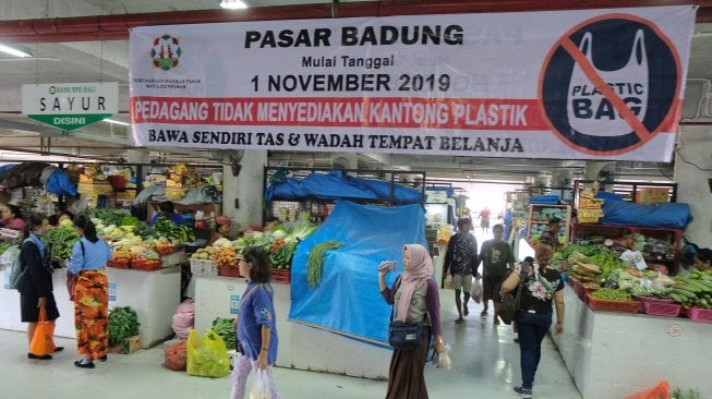 Pengunjung melintas di dekat spanduk larangan kantong plastik belanjaan di Pasar Badung, Denpasar, Bali.