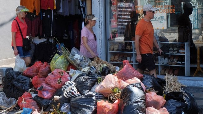 Wisatawan mancanegara melintas di dekat tumpukan sampah di kawasan pertokoan di Kuta, Badung.