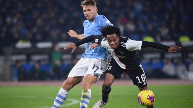 Gelandang Juventus Juan Cuadrado menahan striker Lazio Ciro Immobile selama pertandingan sepak bola Serie A Italia, Lazio melawan Juventus di stadion Olimpico, Roma, Italia, Minggu (8/12) dini hari WIB. [Filippo MONTEFORTE / AFP]
