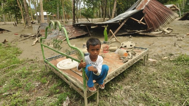 Seorang anak berada disekitar rumahnya yang rusak dan terendam lumpur akibat diterjang banjir bandang di Desa Poi, Kabupaten Sigi, Sulawesi Tengah, Minggu (8/12).  [ANTARA FOTO/Mohamad Hamzah]