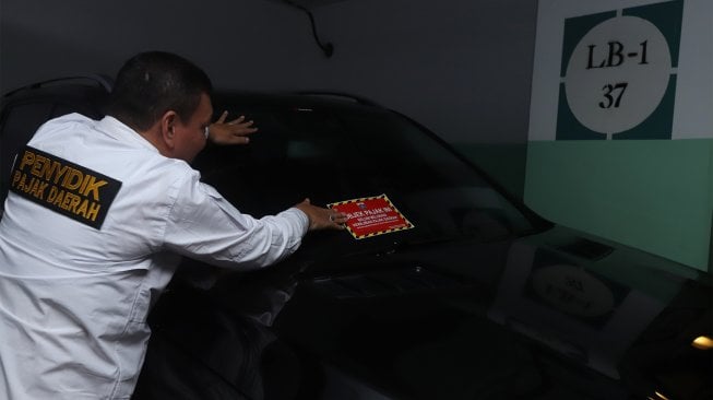 Petugas Samsat Jakarta Pusat menempelkan stiker 'Objek Pajak' pada mobil mewah saat razia supervisi pencegahan pajak mobil mewah di Apartemen Pavilion, Jakarta Pusat, Senin (9/12). [Suara.com/Angga Budhiyanto]