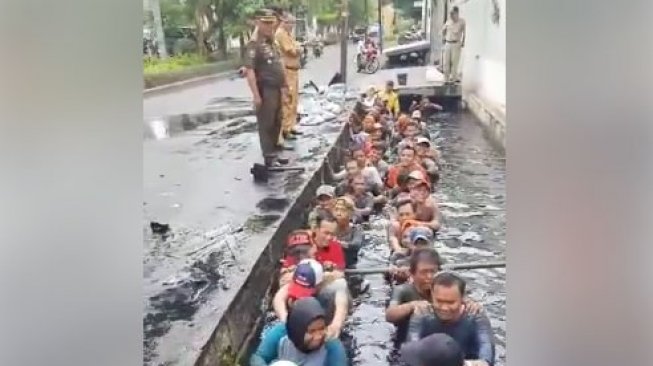Video pegawai honorer di Jakarta Barat masuk ke got berisi air keruh dan kotor ketika melakukan tes perpanjangan kontrak, viral di media-media sosial. [Facebook]