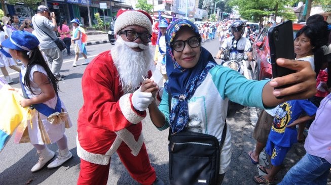 Seorang wanita berhijab berswafoto bersama peserta dengan kostum sinterklas saat Salatiga Christmas Parade di Salatiga, Jawa Tengah, Sabtu (14/12). [ANTARA FOTO/Aloysius Jarot Nugroho]