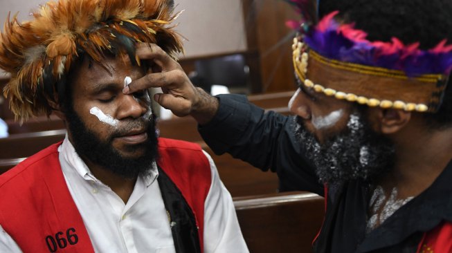 Terdakwa kasus makar Dano Tabuni (kanan) melukis wajah terdakwa Ambrosius Mulait sebelum dimulainya sidang di Pengadilan Negeri Jakarta Pusat, Jakarta, Senin (16/12). [ANTARA FOTO/Aditya Pradana Putra]