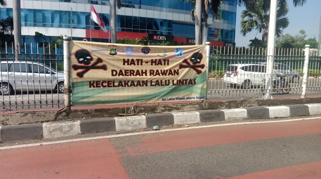 Spanduk bertuliskan hati-hati rawan kecelakaan. (Suara.com/Yosea Arga)