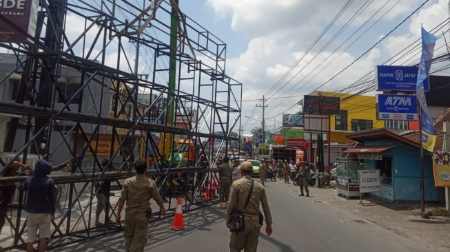 Petugas Satpol PP Kabupaten Sleman melakukan pembongkaran baliho raksasa yang melintang di Jalan Kaliurang, Selasa (17/12/2019). [Istimewa]