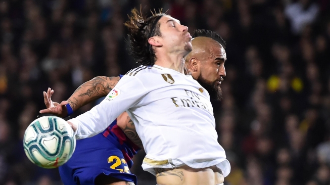 Bek Real Madrid Sergio Ramos dan pemain tengah Barcelona Arturo Vidal melompat untuk merebut bola selama pertandingan sepak bola Liga Spanyol "El Clasico" antara Barcelona melawan Real Madrid di Camp, Barcelona, Spanyol, Kamis (18/12) dini hari WIB.  [JOSE JORDAN / AFP]