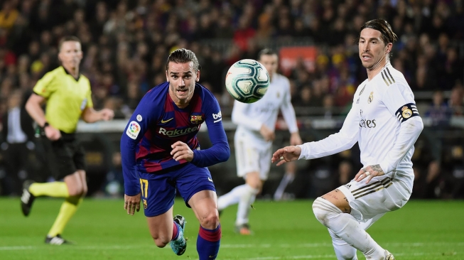 Pemain depan Barcelona Antoine Griezmann (tengah) dan pemain belakang Real Madrid Sergio Ramos memperhatikan bola selama pertandingan sepak bola Liga Spanyol "El Clasico" antara Barcelona melawan Real Madrid di Camp, Barcelona, Spanyol, Kamis (18/12) dini hari WIB. [JOSE JORDAN / AFP]