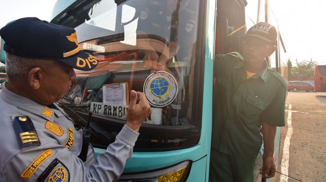 Petugas Dinas Perhubungan DKI Jakarta memasang stiker lulus inspeksi saat pemeriksaan kelaikan angkutan di Terminal Kampung Rambutan, Jakarta, Jumat (20/12). [ANTARA FOTO/Indrianto Eko Suwarso]