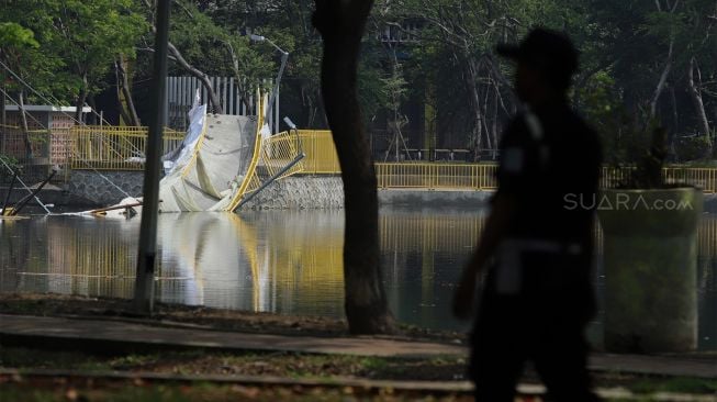 Petugas keamanan melakukan penjagaan di sekitar jembatan lengkung yang roboh di hutan kota Kemayoran, Jakarta Pusat, Senin (23/12). [Suara.com/Angga Budhiyanto]