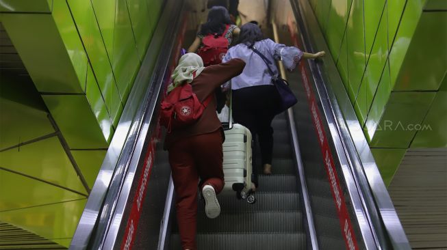 Sejumlah calon penumpang menaiki eskalator menuju kereta api di Stasiun Gambir, Jakarta Pusat, Senin (23/12). [Suara.com/Angga Budhiyanto]  