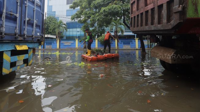 Petugas membersihkan sampah di jalan yang terendam banjir di kawasan Sunter, Jakarta Utara, Rabu (25/12). [Suara.com/Angga Budhiyanto]