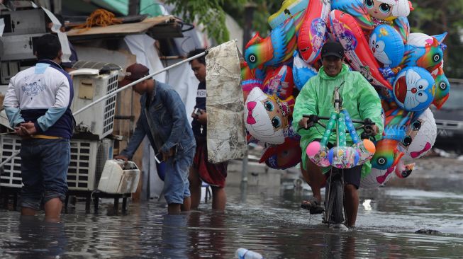 Pedagang balon melintas di jalan yang terendam banjir di kawasan Sunter, Jakarta Utara, Rabu (25/12). [Suara.com/Angga Budhiyanto]
