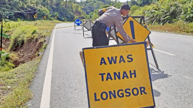 Seorang anggota Polsek Entikong memasang papan peringatan di lokasi jalan lintas negara yang mengalami retak akibat tanah longsor di perbatasan Entikong, Kabupaten Sanggau, Kalimantan Barat, Kamis (26/12). [ANTARA FOTO/Agus Alfian]