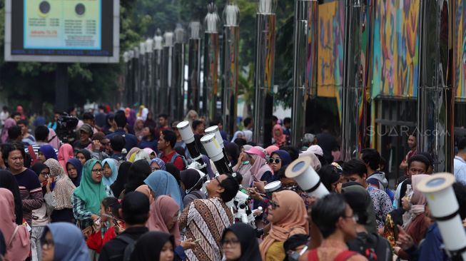 Pengunjung menggunakan teleskop untuk melihat gerhana matahari cincin dari Planetarium Taman Ismail Marzuki, Jakarta, Kamis (26/12). [Suara.com/Angga Budhiyanto]
