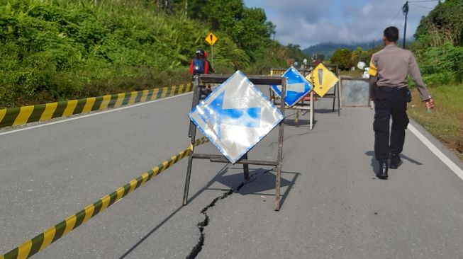 Polisi memasang papan peringatan di jalan raya yang mengalami retak di perbatasan Entikong, Kabupaten Sanggau, Kalimantan Barat, Kamis (26/12). [ANTARA FOTO/Agus Alfian]