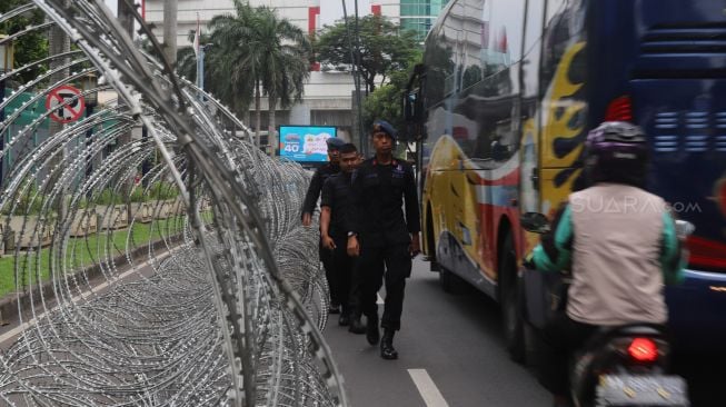 Polisi melintas di samping kawat berduri untuk menghalau pengunjuk rasa di depan Kedutaan Besar Republik Rakyat China, Kuningan, Jakarta Selatan, Jumat (27/12). [Suara.com/Alfian Winanto]