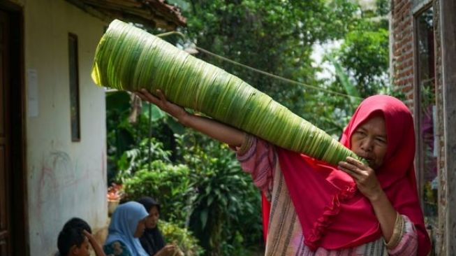 Nini Tarsih meniup terompet turutu raksasa hasil buatannya sendiri di Desa Karanglo, Kecamatan Cilongok, Kabupaten Banyumas, Kamis (26/12/2019). (Suara.com/Anang Firmansyah)