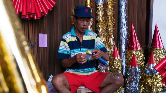 Pak Lantur yang sedang membuat terompet di lapaknya di daerah Glodok, Jakarta Barat, Minggu (29/12). (suara.com/Alfian Winanto)

