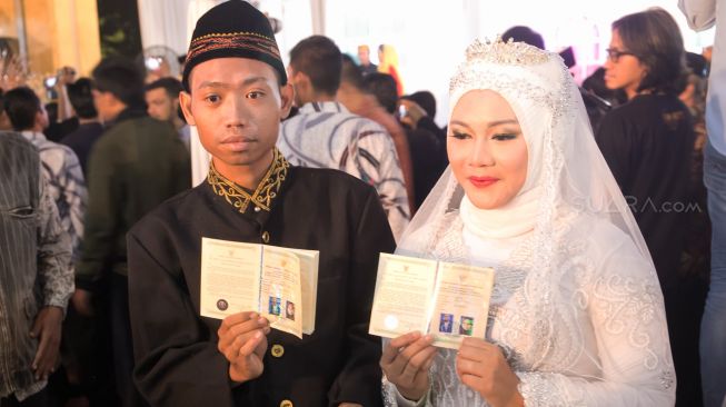 Pasangan nikah Masaal yang menunjukkan buku Nikah nya di acara nikah massal yang ada di Balaikota, Gambir, Jakarta Pusat, Selasa (31/12). [Suara.com/Alfian Winanto]