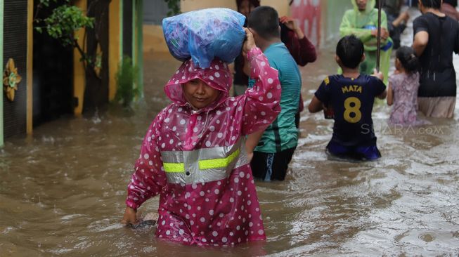 Sejumlah warga melintasi jalan yang terendam banjir di kawasan Jatipadang, Pasar Minggu, Jakarta Selatan, Rabu (1/1). [Suara.com/Angga Budhiyanto]