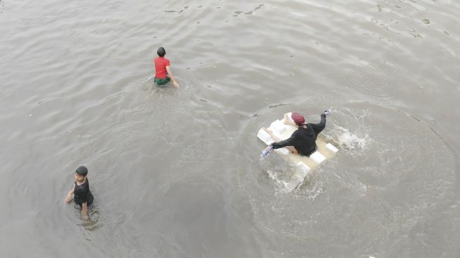 Sejumlah bocah bermain saat banjir yang merendam Jalan Letjen S Parman dan tol dalam kota di Jakarta Barat, Rabu (1/1). [ANTARA FOTO/Nova Wahyudi]

